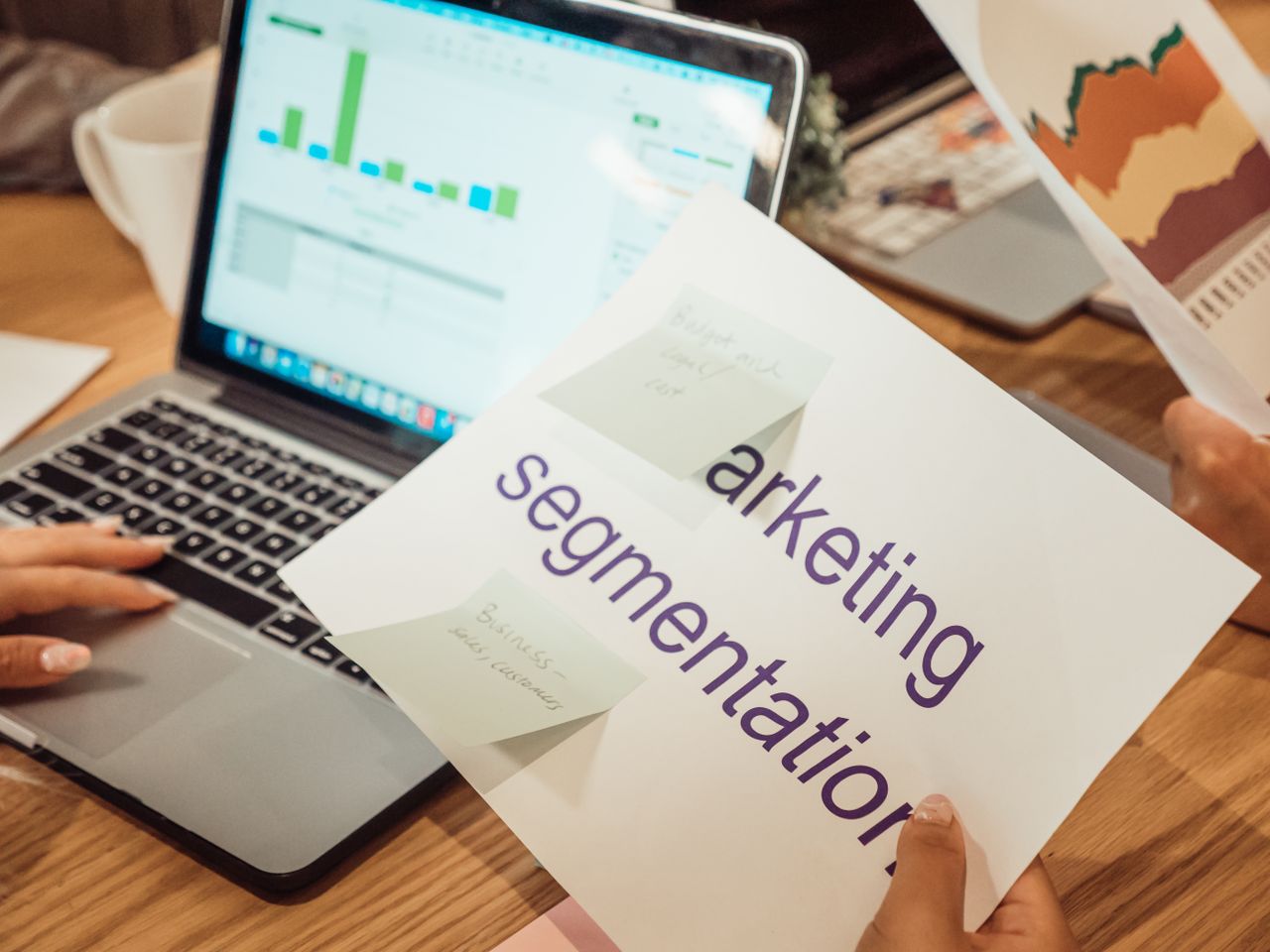 Un espace de travail moderne où l'on voit des mains analyser des données marketing sur un ordinateur portable et des documents papier.